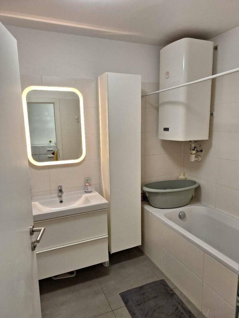 Funktionales Badezimmer mit Badewanne, Einzelwaschbecken und beleuchtetem Spiegel.
