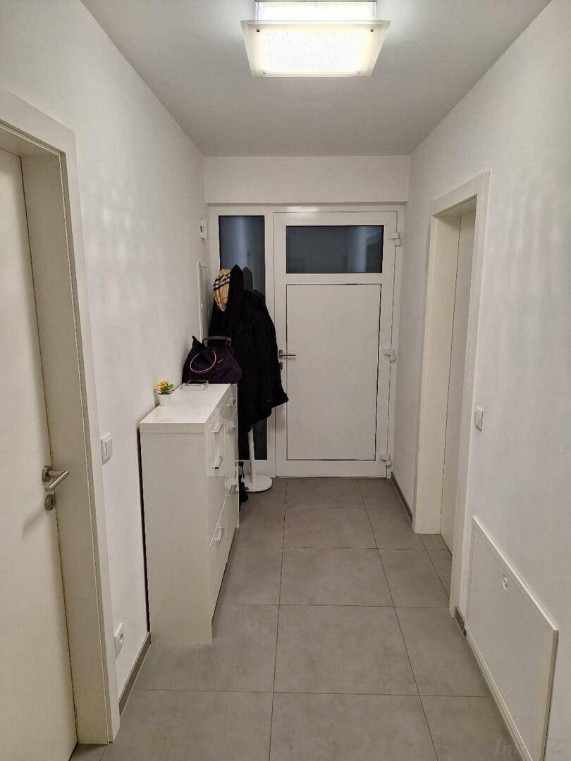 Heller Eingangsbereich mit Fliesenboden, Garderobe und weißer Kommode.