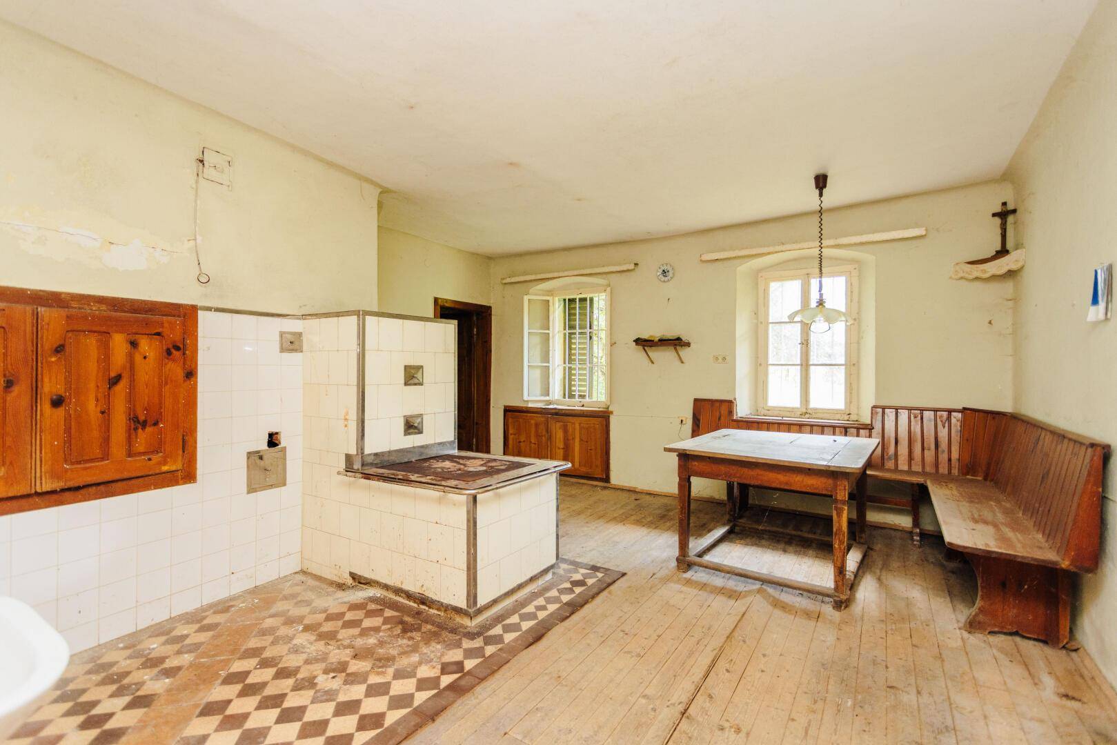 Rustikale Küche mit einem traditionellen Holzofen, Holzdielenboden und einem einfachen Esstisch.