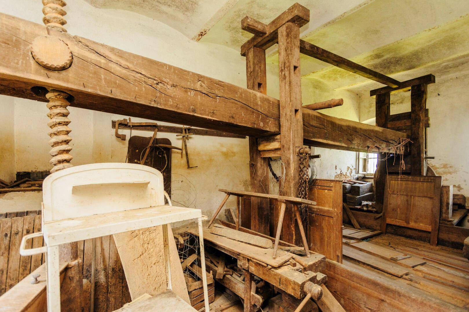Historischer Raum mit großen Holzbalken und einer alten Presse, der die landwirtschaftliche Vergangenheit des Hofes zeigt.