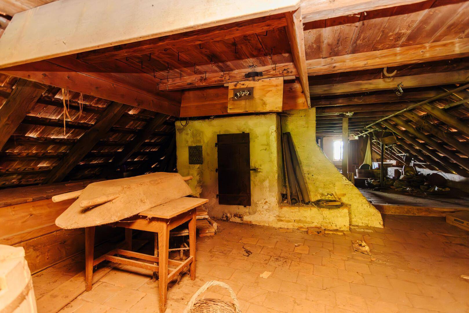 Dachboden mit sichtbaren Holzbalken, Ziegelboden und alten Möbeln, der viel Stauraum bietet.