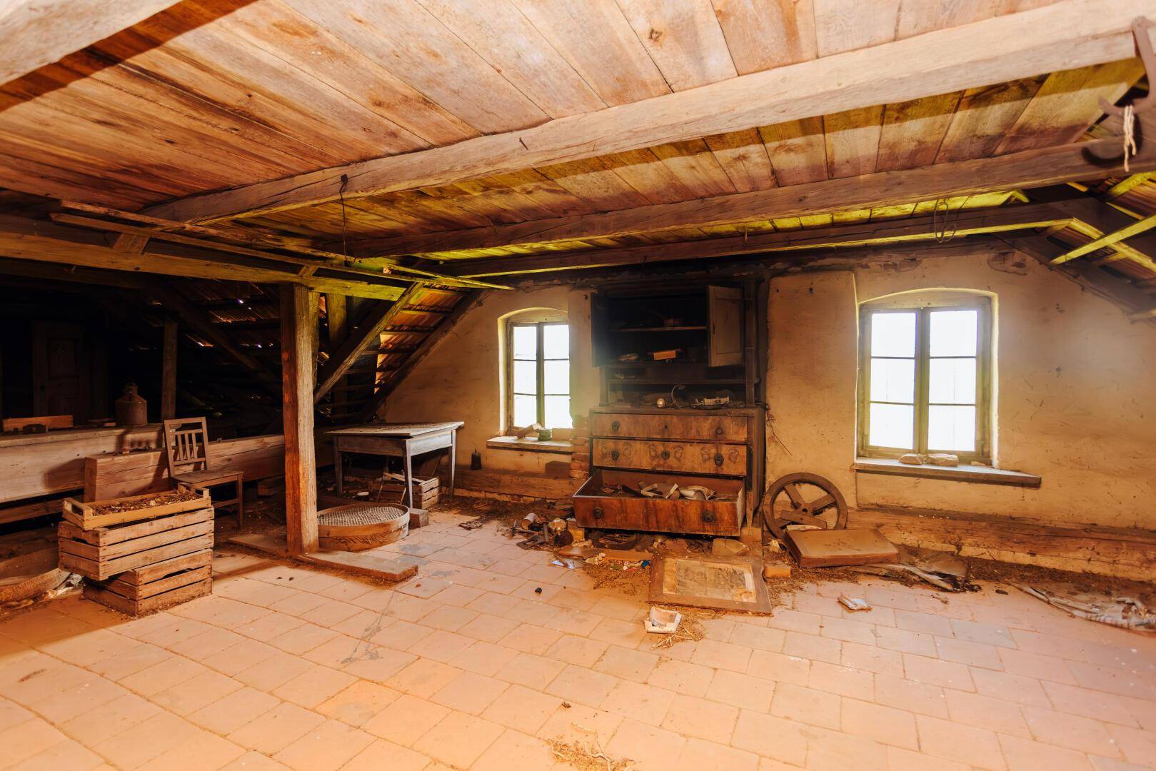 Dachboden mit Holzbalken, Ziegelboden und alten Möbeln, der das Potenzial für einen Ausbau zeigt.