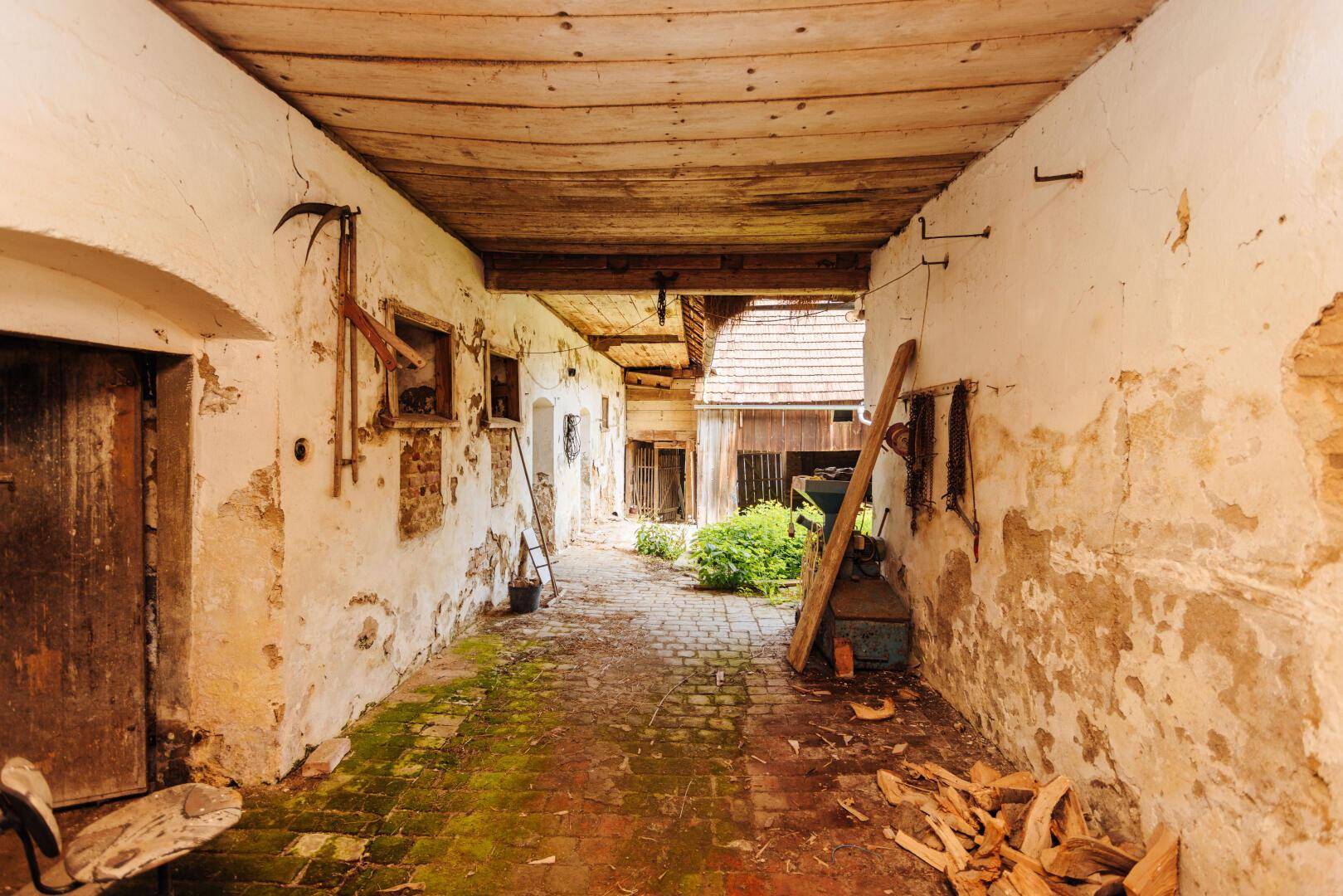 Historischer Durchgang mit verputzten Wänden und Holzbalkendecke, der zu einem hellen Außenbereich führt.