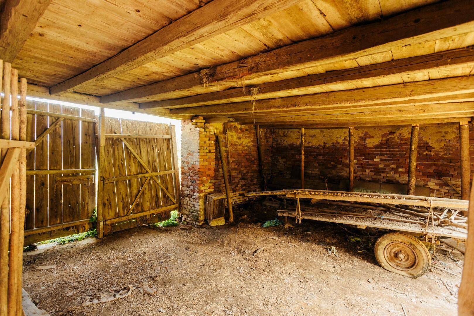 Geräumiger Scheunenbereich mit Holzbalkendecke und einem großen Holztor, das ins Freie führt.