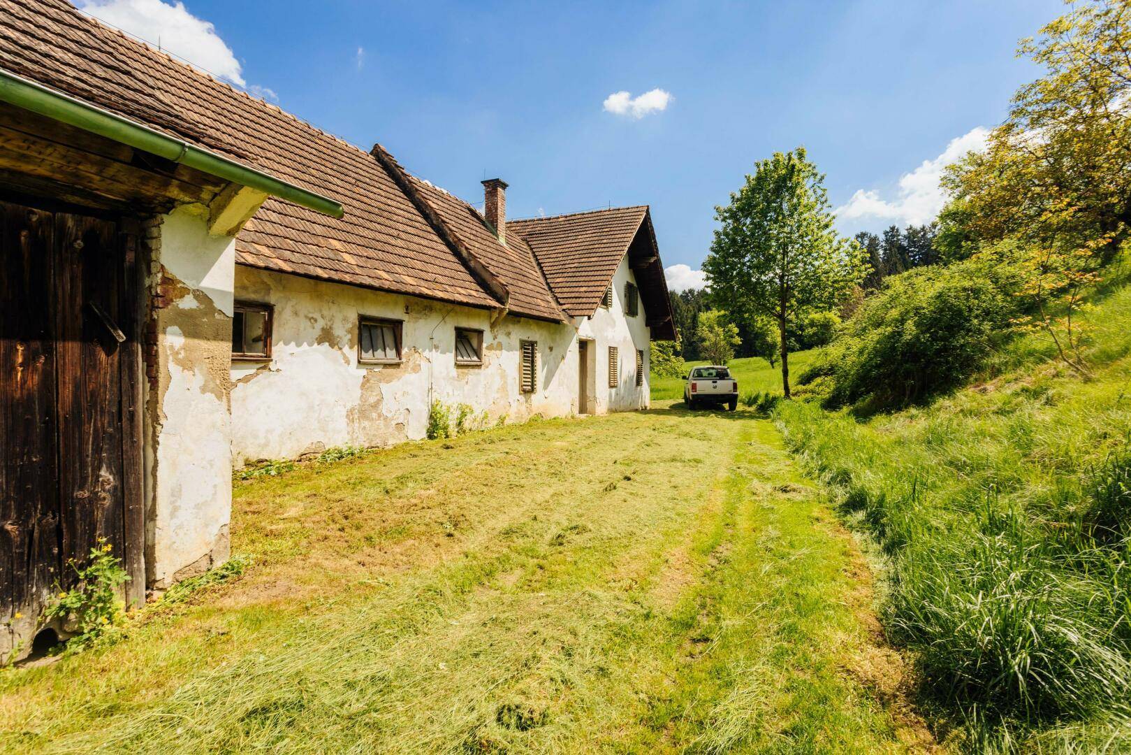 Ansicht des Bauernhofs mit verputzten Wänden und einem Weg, der zu den Gebäuden führt, umgeben von Gras.