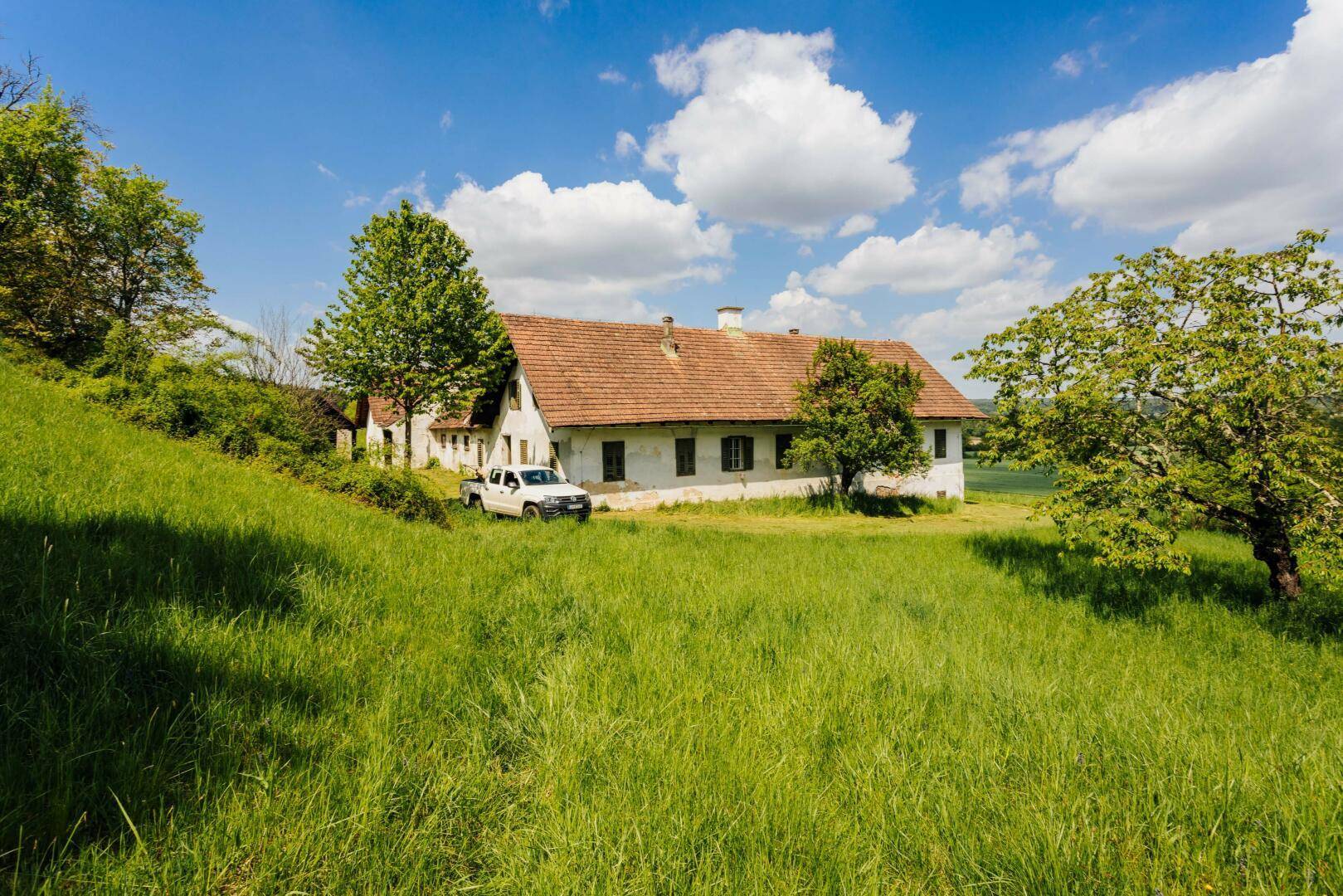 Ansicht des Hauptgebäudes eines Bauernhofs mit weiß getünchten Wänden und einem roten Ziegeldach in ländlicher Umgebung.