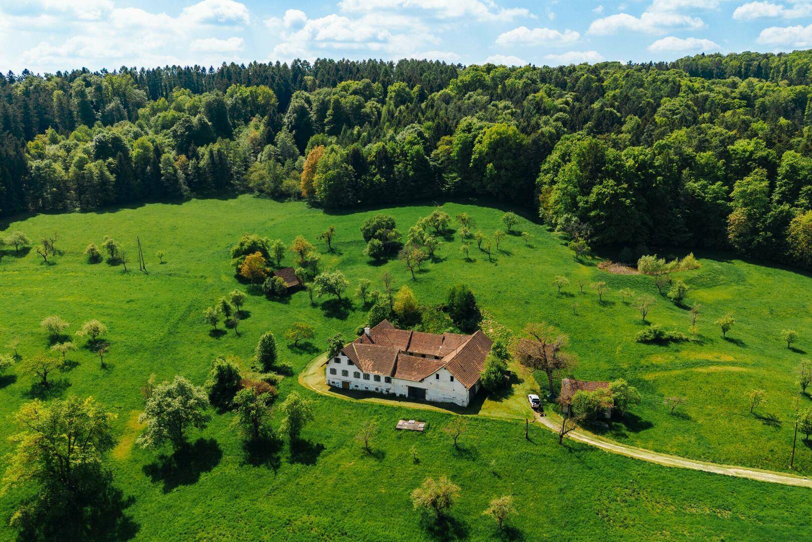 Weitwinkel-Luftaufnahme eines Bauernhofs in einer malerischen ländlichen Umgebung mit Feldern und Wald.