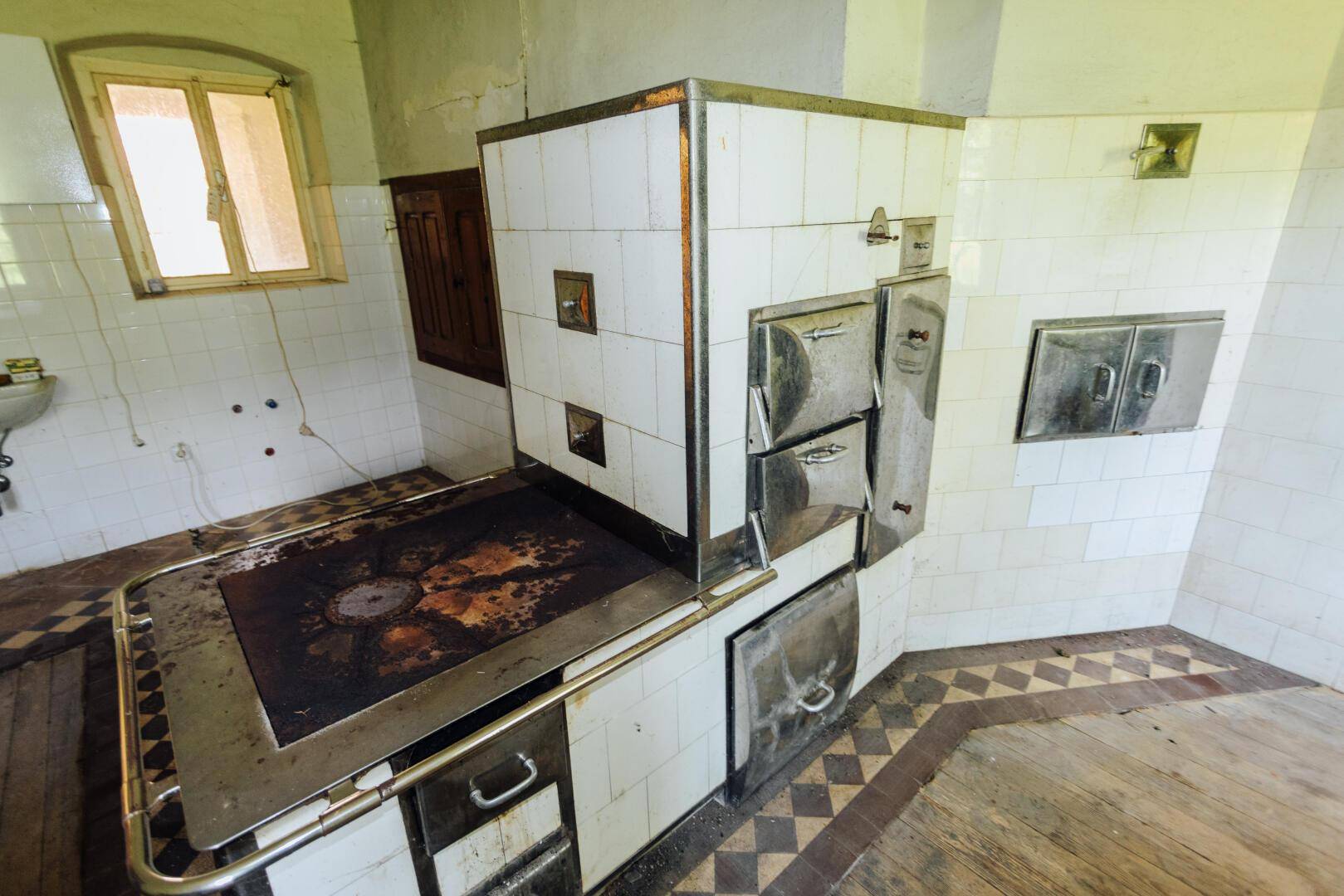 Detailansicht eines großen, gefliesten Holzofens mit Metalltüren in einer traditionellen Küche.
