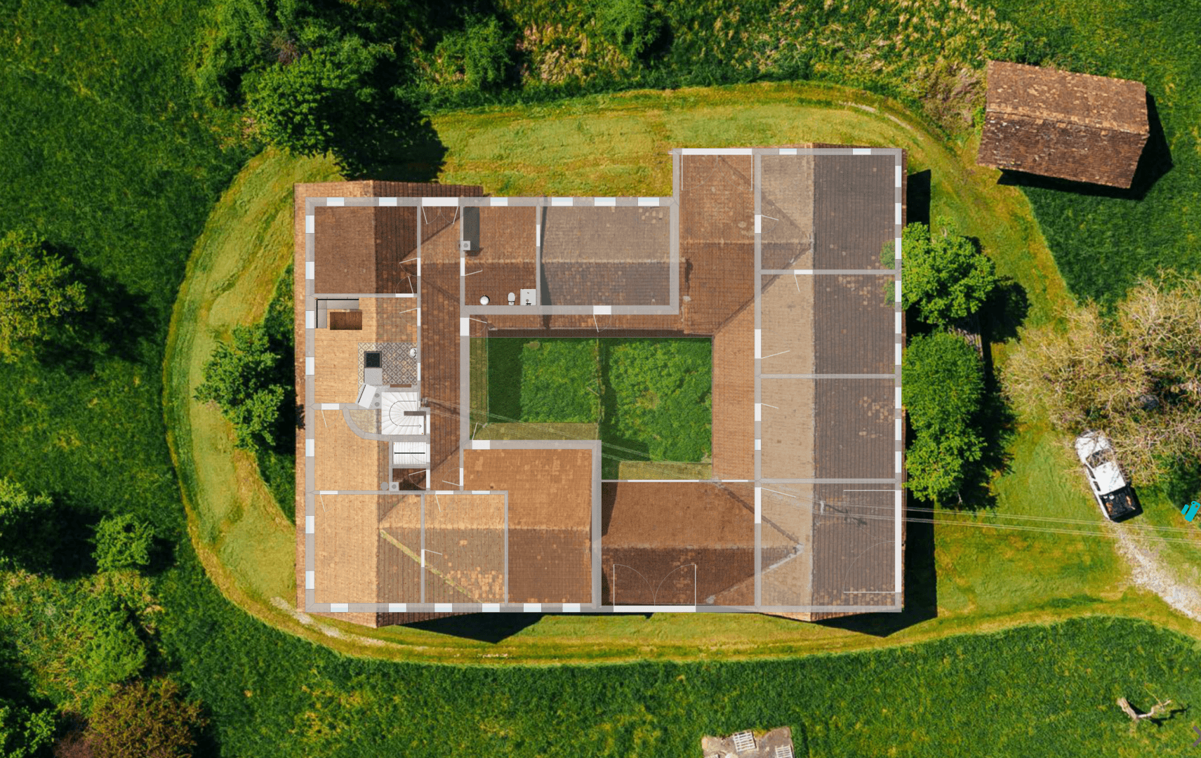 Luftaufnahme eines Gebäudes mit überlagertem Grundriss, umgeben von viel Grün und einem zentralen Innenhof.