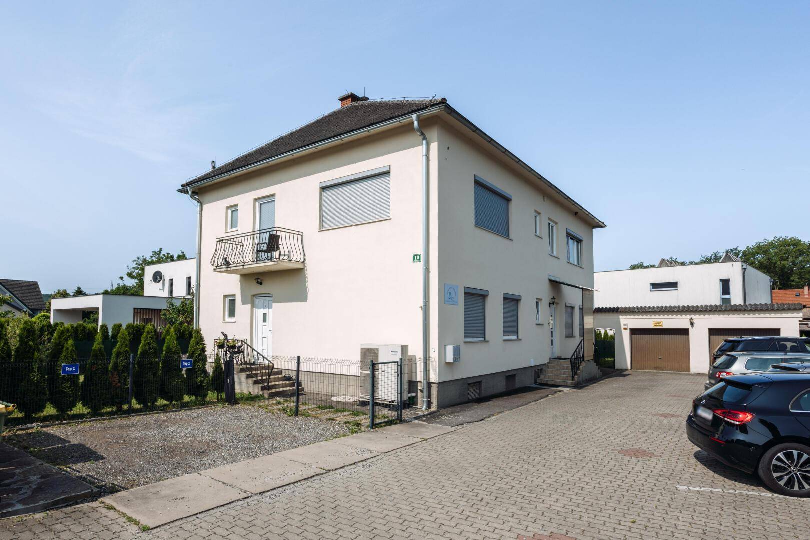 Vorderansicht des Hauses mit Zufahrt, Parkplätzen und Garagen im Hintergrund.