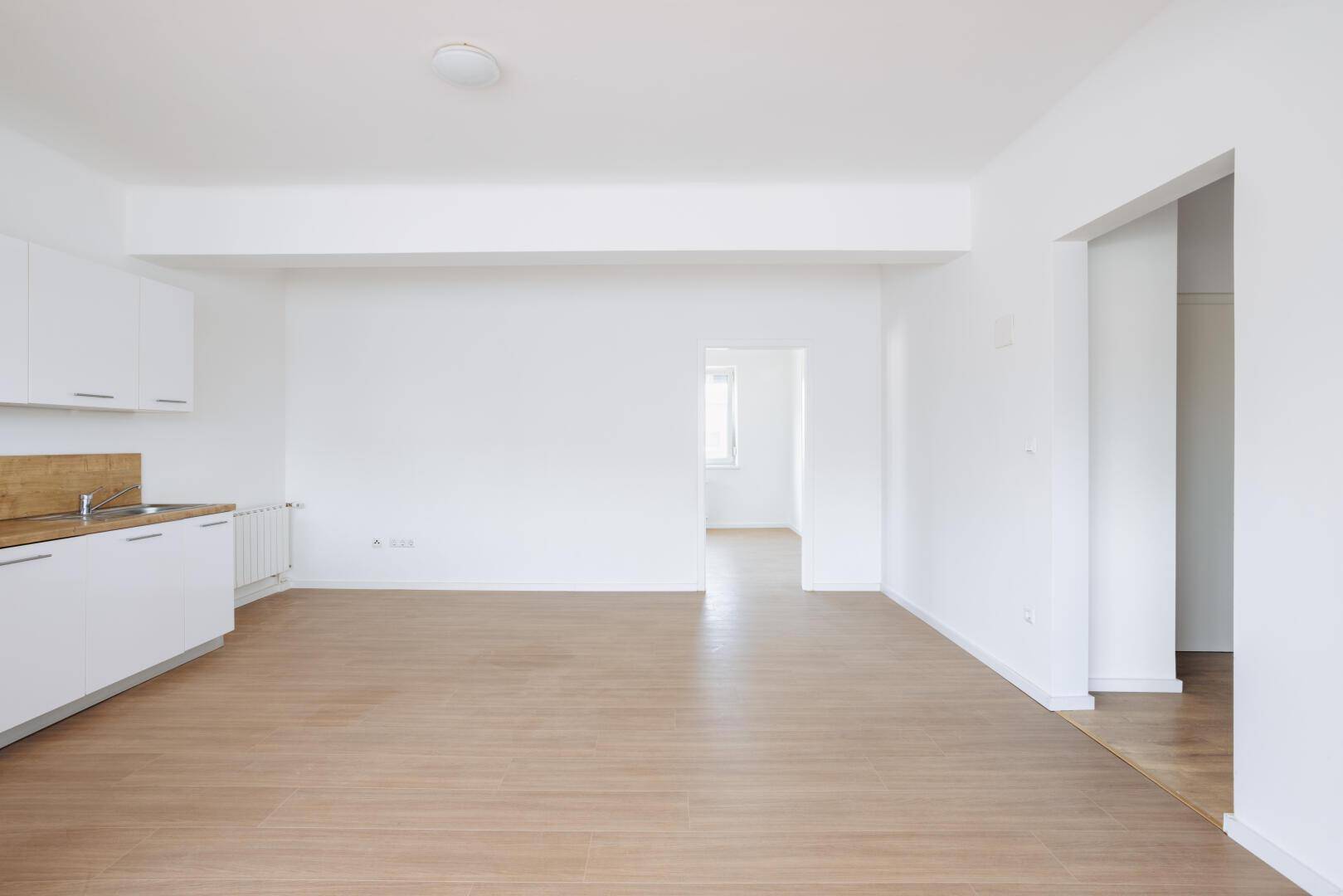 Offener Wohnbereich mit Küchenzeile, Laminatboden und Zugang zu weiteren Räumen.