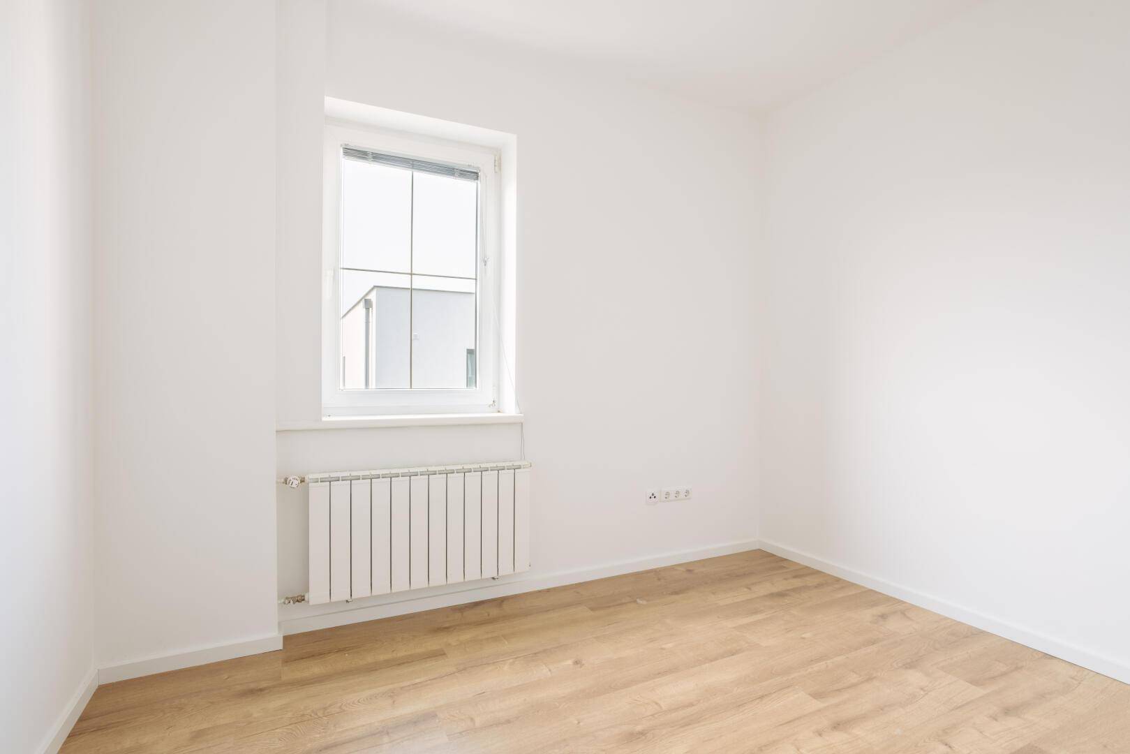 Helles Zimmer mit Laminatboden, weiß gestrichenen Wänden und einem Fenster für Tageslicht.