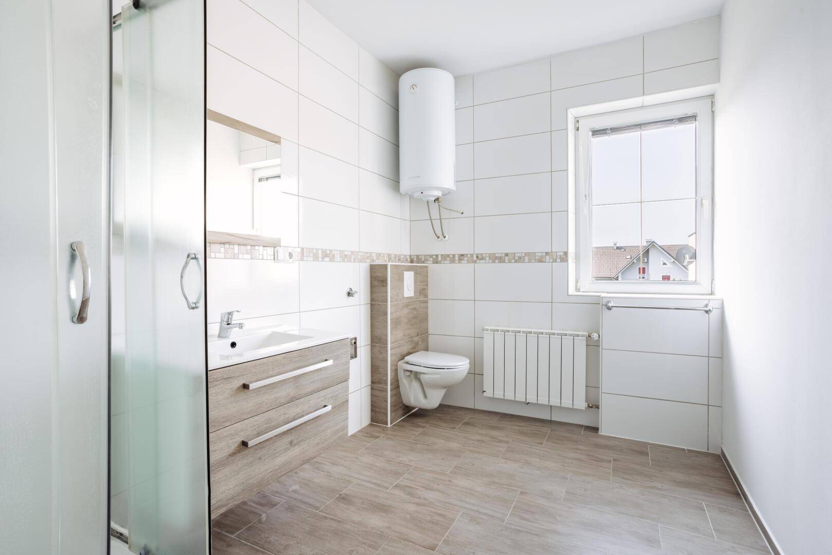 Helles Badezimmer mit Duschkabine, WC, Waschbecken und Fenster für natürliches Tageslicht.