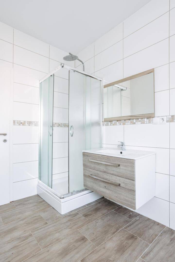 Modernes Badezimmer mit Duschkabine, Waschbecken und hellen Fliesen an Wänden und Boden.