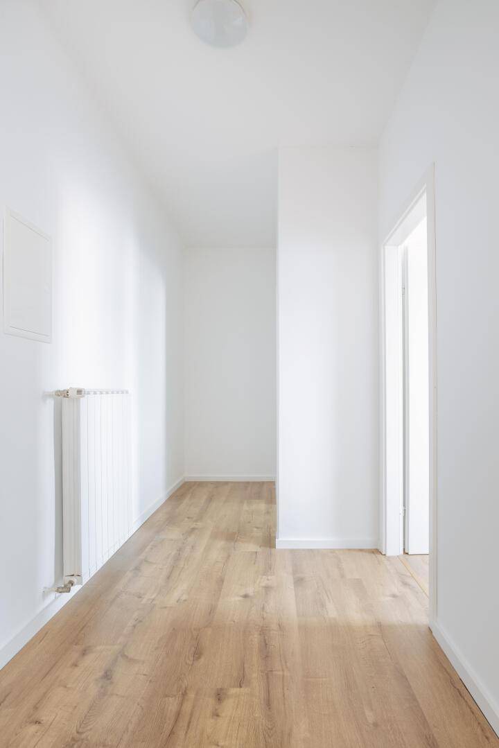 Langer, heller Flur mit Laminatboden und weiß gestrichenen Wänden.