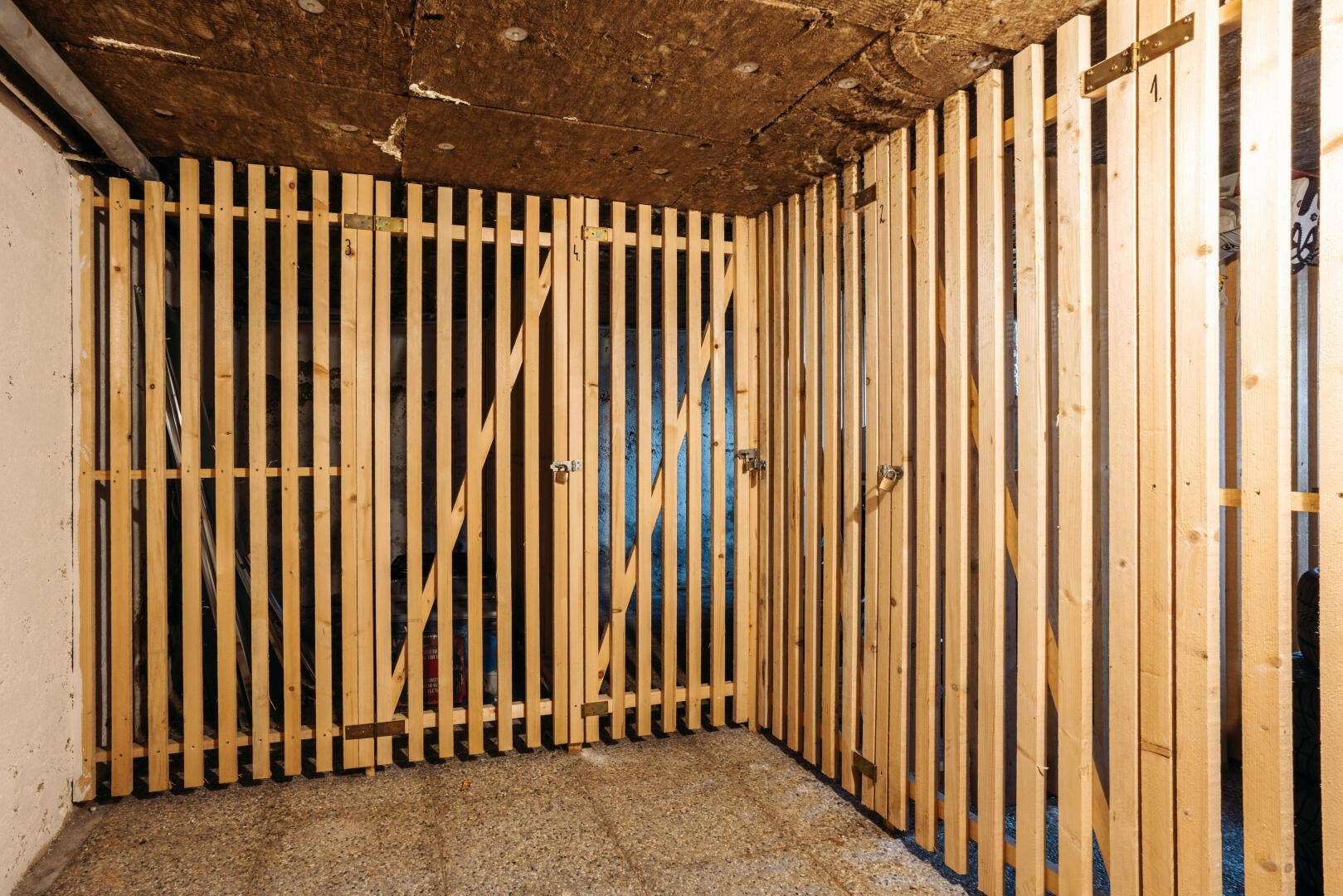 Abstellraum im Keller mit Holzlattenverschlägen für individuelle Lagerung und Organisation.