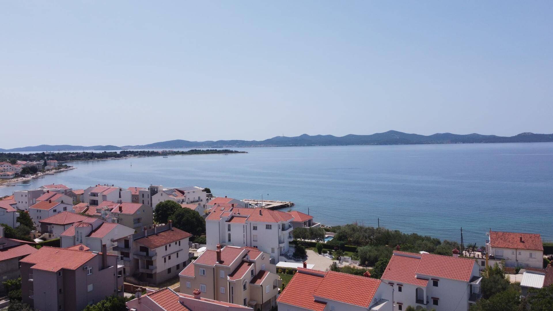 Panoramablick auf die Küstenstadt mit roten Dächern, dem Meer und den fernen Bergen.