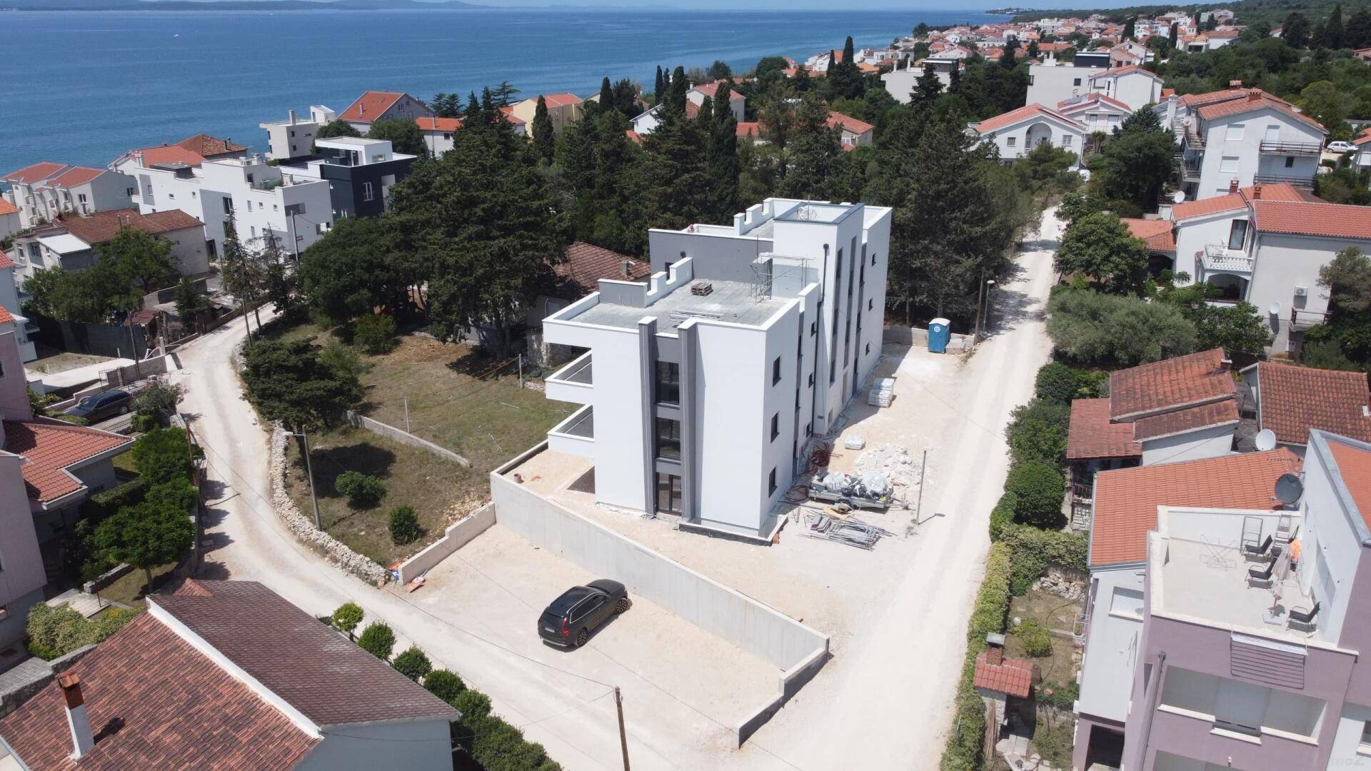 Luftaufnahme des modernen Apartmentgebäudes im Bau mit Meerblick und geparktem Fahrzeug.