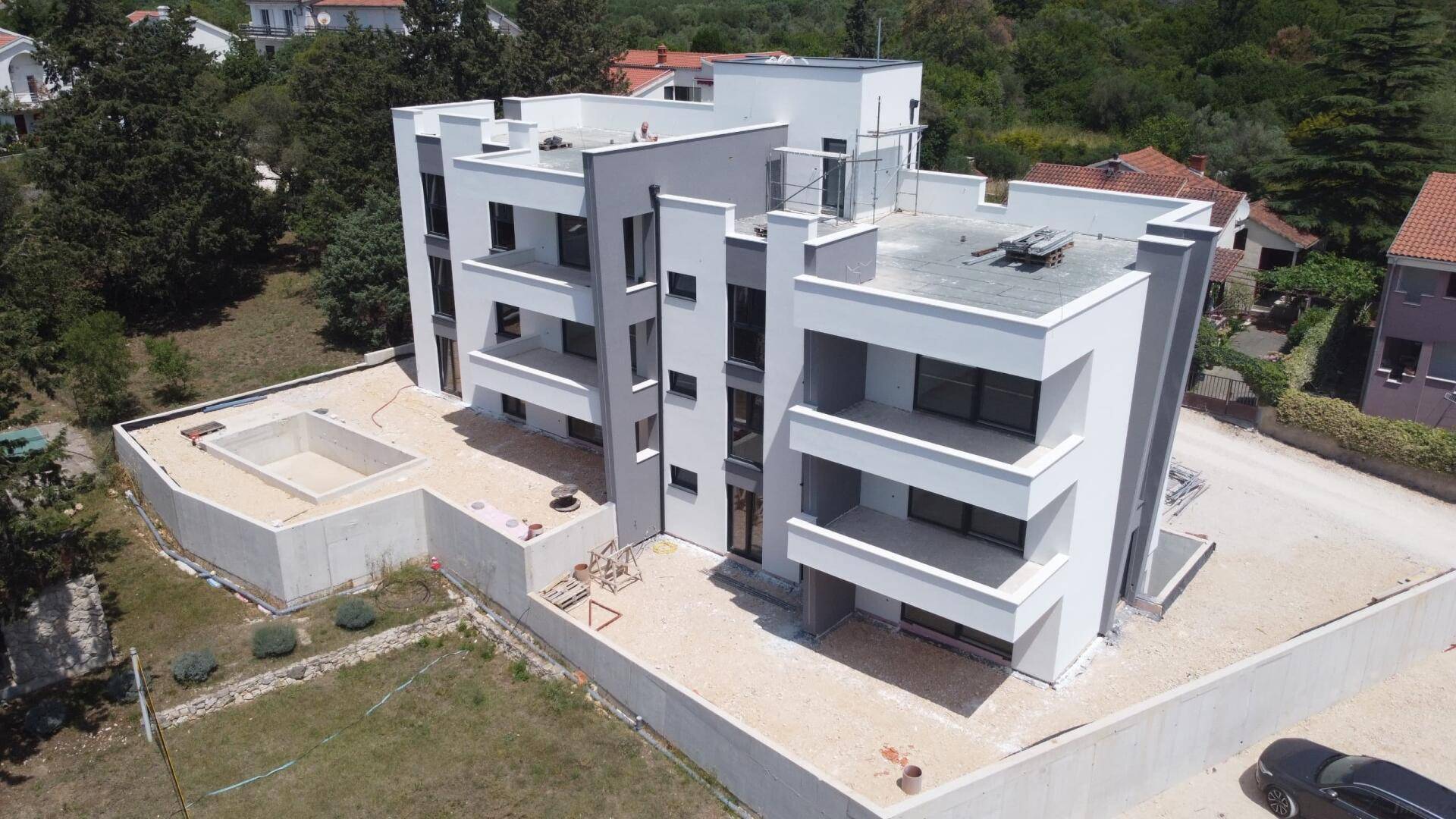 Ansicht des modernen Apartmentgebäudes im Bau mit unfertigem Pool und umliegendem Gelände.