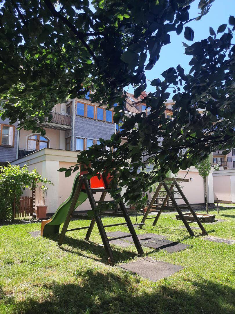 Kinderspielplatz mit Rutsche und Schaukeln in einer grünen Gartenanlage.