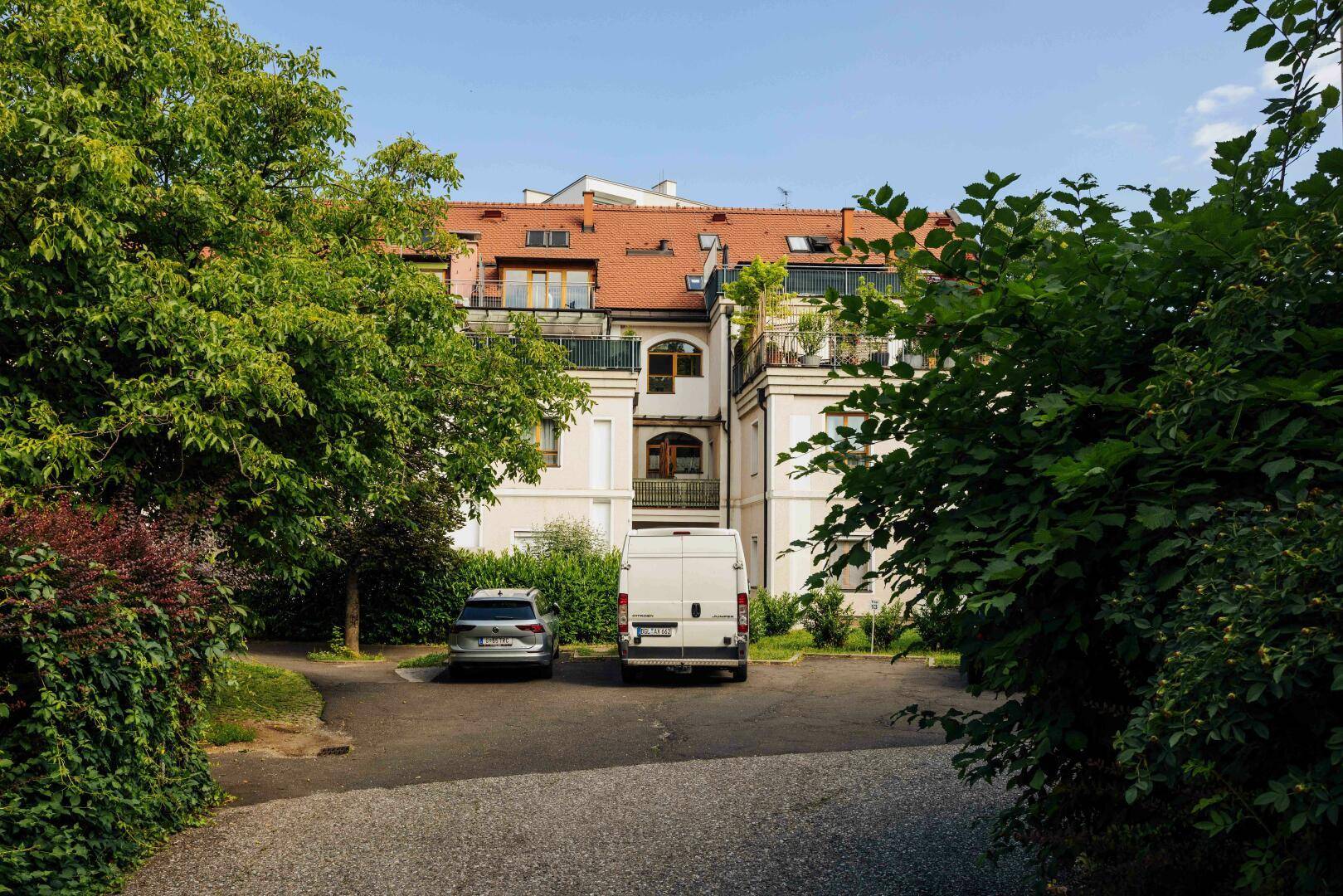 Wohngebäude mit rotem Ziegeldach, Balkonen und Parkplätzen im Grünen.