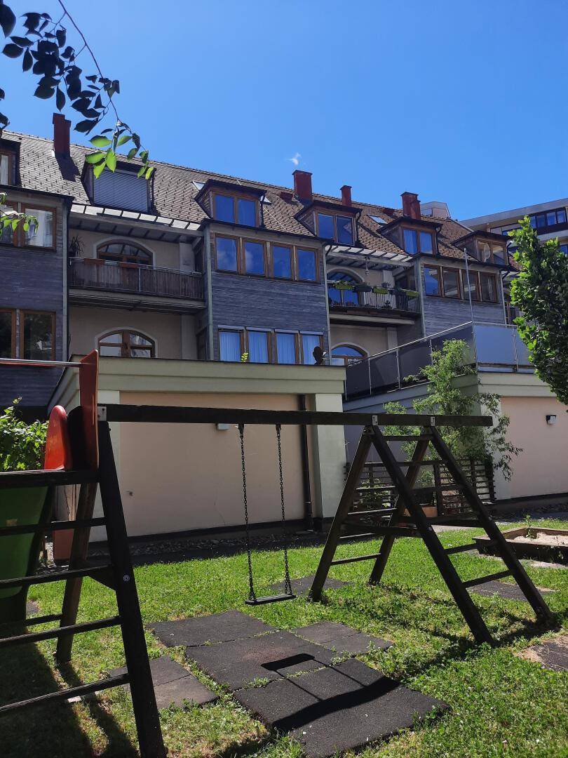 Rückseite des Gebäudes mit mehreren Balkonen und einem Kinderspielplatz im Garten.