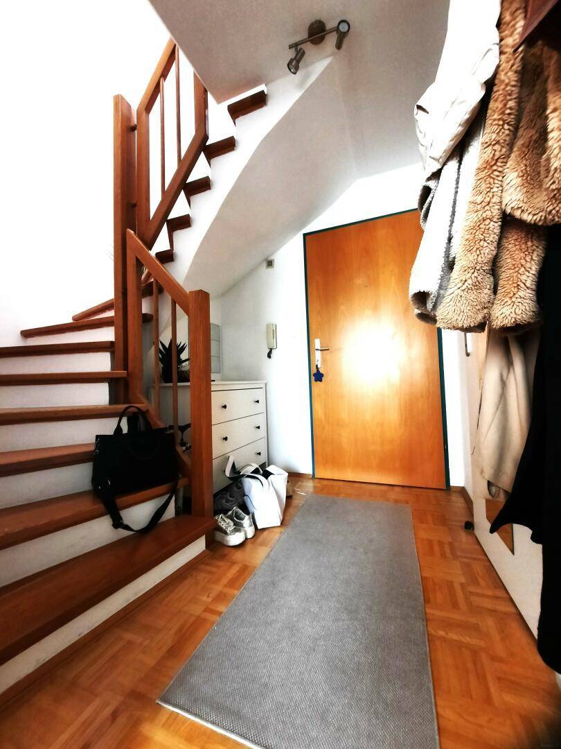 Heller Eingangsbereich mit Holztreppe, Parkettboden und Garderobe.