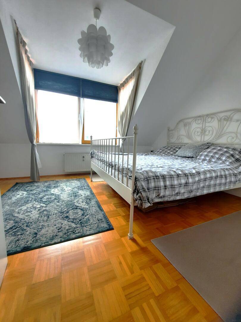 Gemütliches Schlafzimmer im Dachgeschoss mit Holzboden und weißem Metallbett.