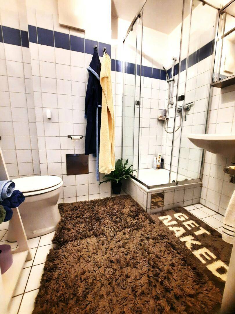 Badezimmer mit Duschkabine, WC und weißen Fliesen mit blauen Akzenten.