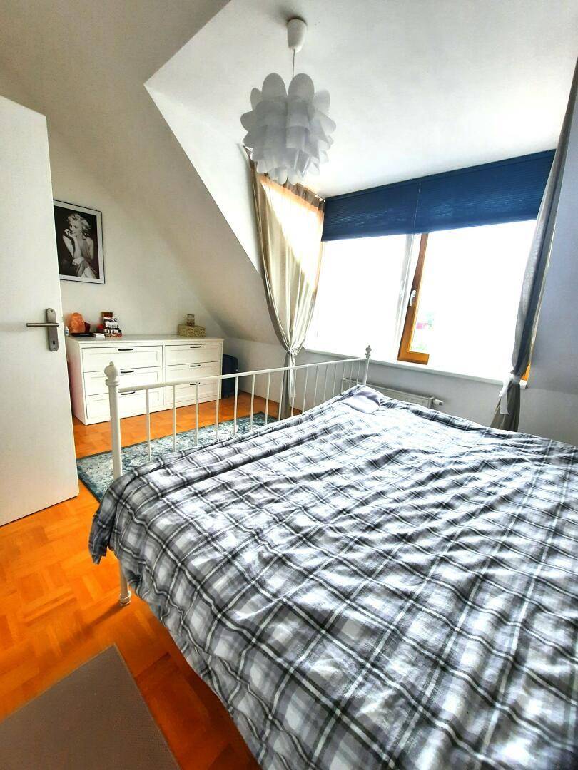 Helles Schlafzimmer mit Dachschräge, Parkettboden und einem großen Fenster.