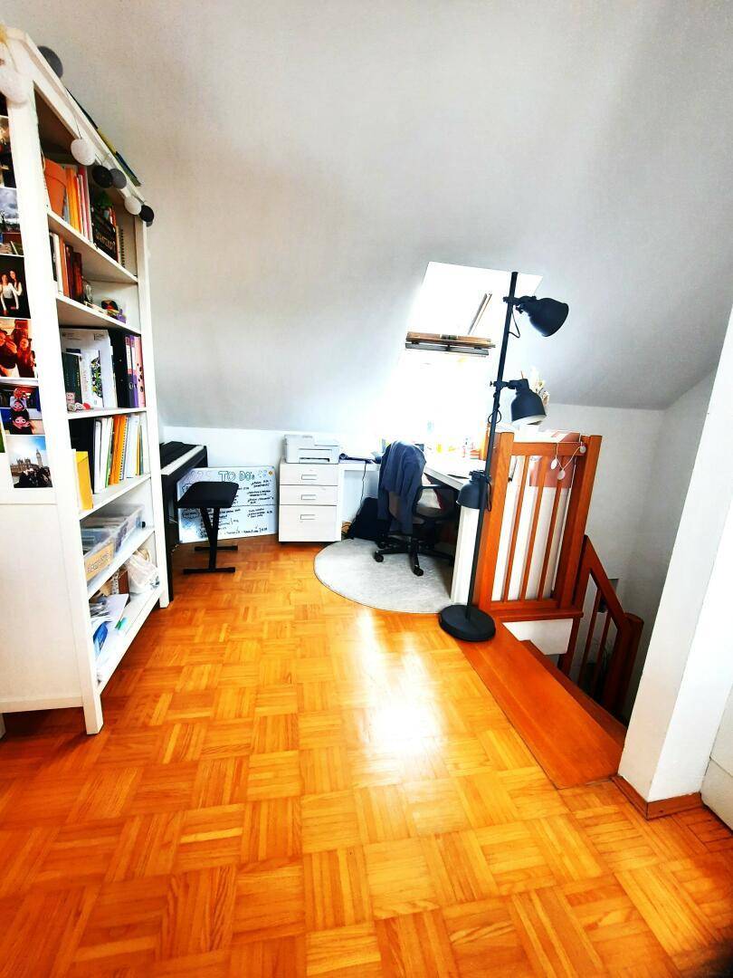Arbeitsbereich im Dachgeschoss mit Bücherregal, Schreibtisch und Parkettboden.