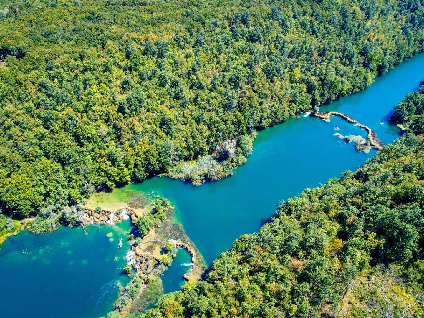 Spektakuläre Luftaufnahme eines Flusses mit Wasserfällen, umgeben von dichtem, grünem Wald.