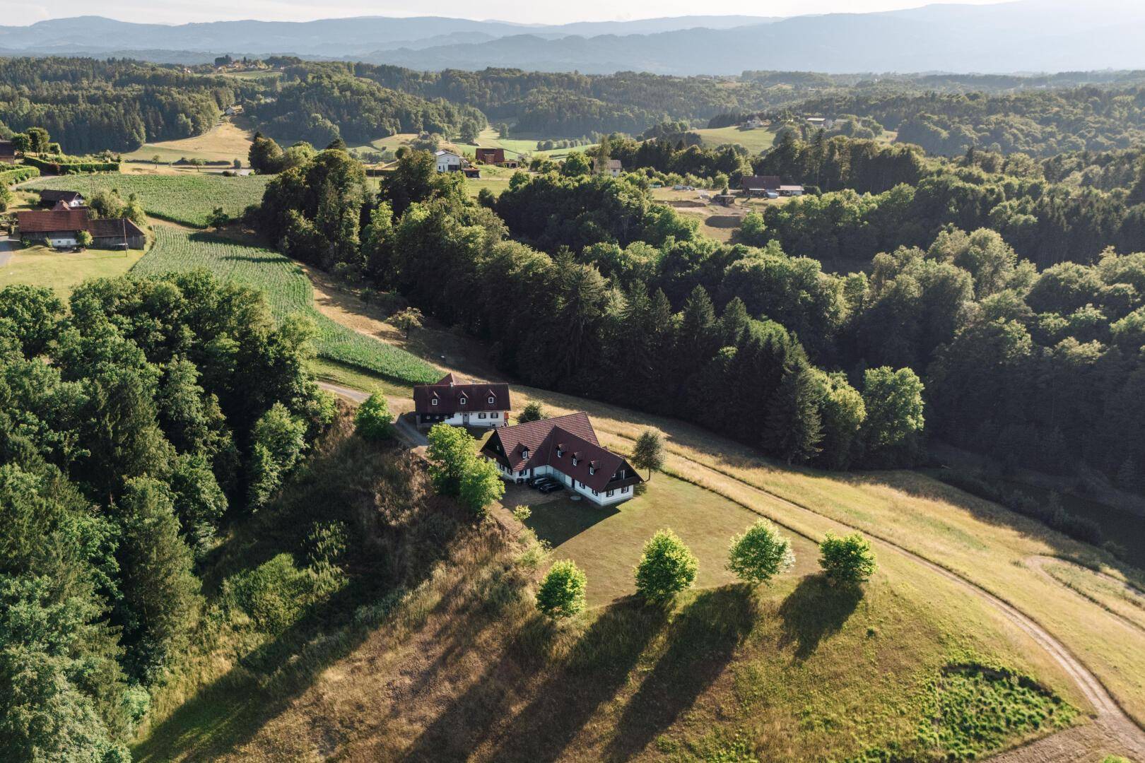 Panoramablick auf die Häuser eingebettet in eine hügelige, bewaldete Landschaft unter blauem Himmel.