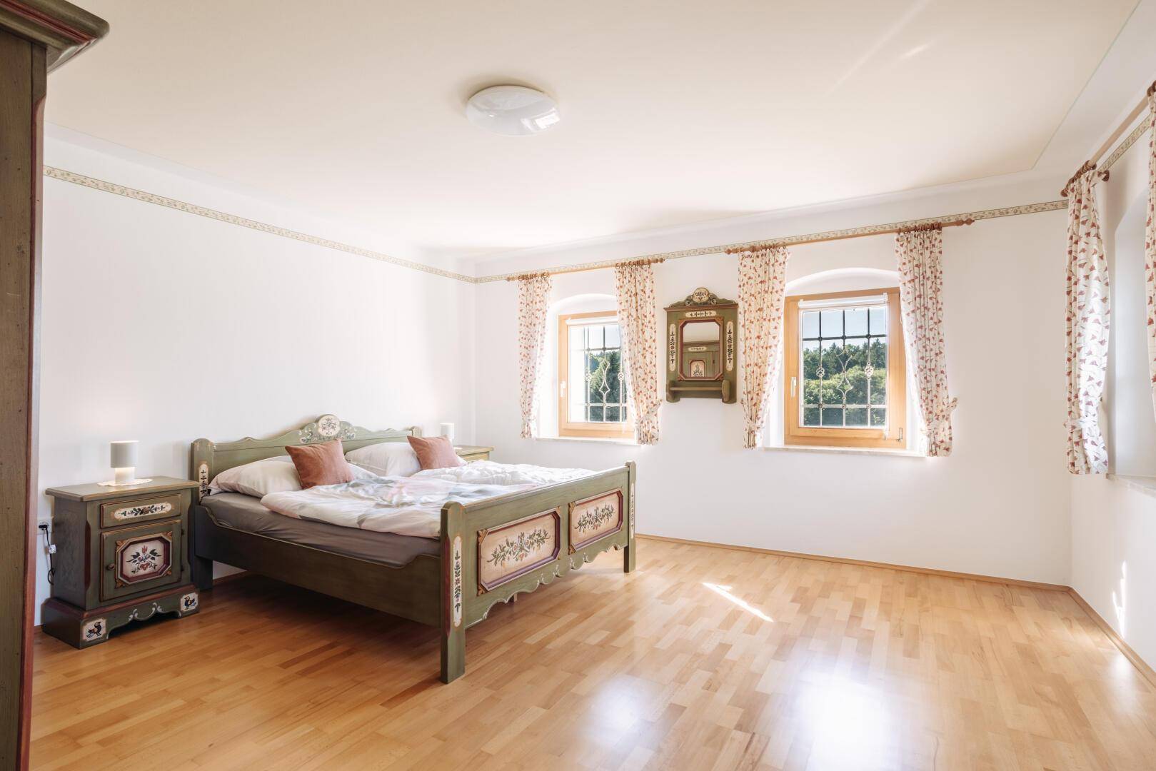 Helles Schlafzimmer mit traditionellem Holzbett, Parkettboden und Blick ins Grüne.