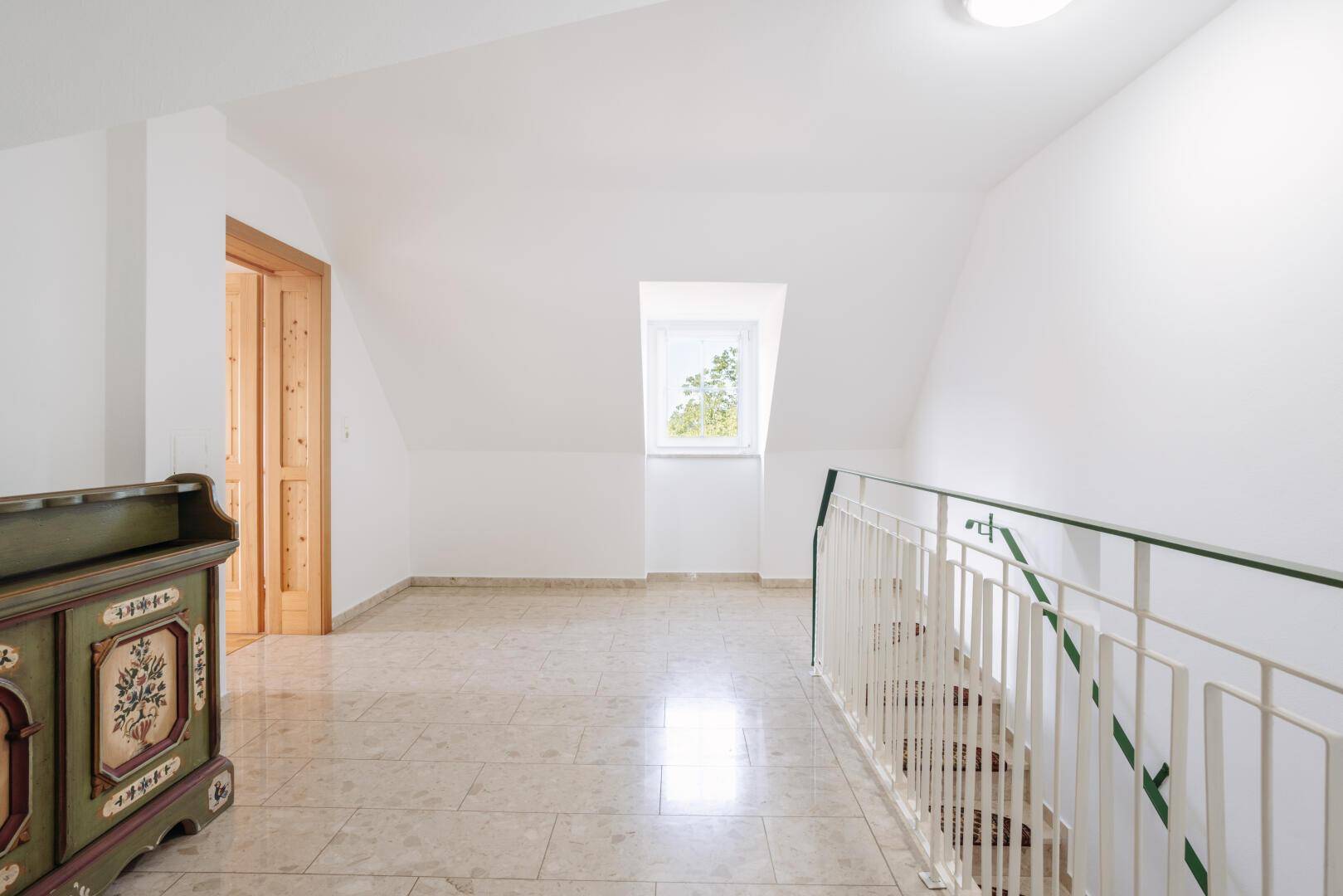 Heller Flur im Dachgeschoss mit Dachfenster, Fliesenboden und Treppengeländer.