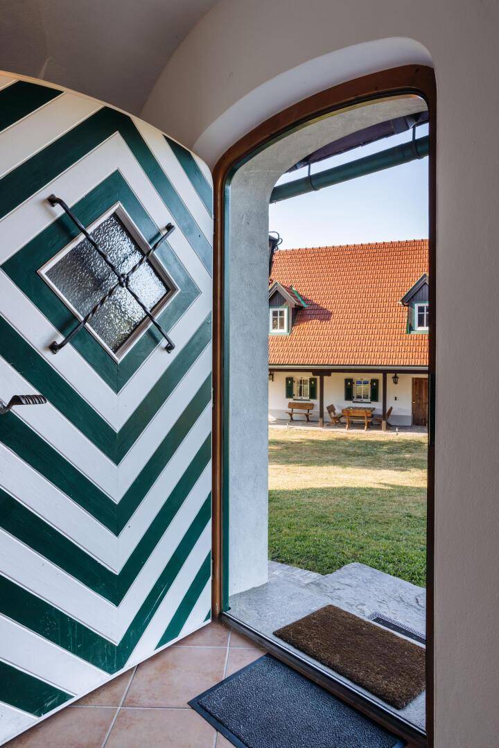 Blick durch die geöffnete Eingangstür auf den gepflegten Garten und das gegenüberliegende Haus.