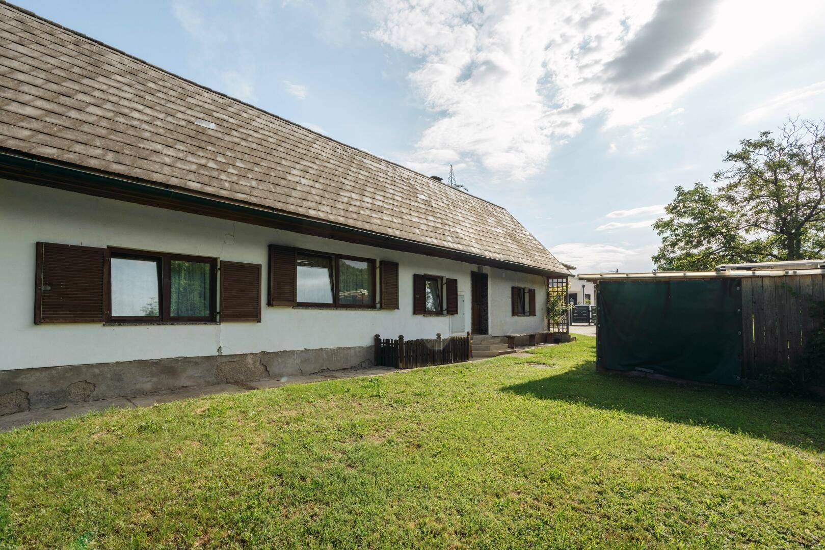 Längliche Hausfassade mit braunen Fensterläden und einem gepflegten Rasenbereich daneben.