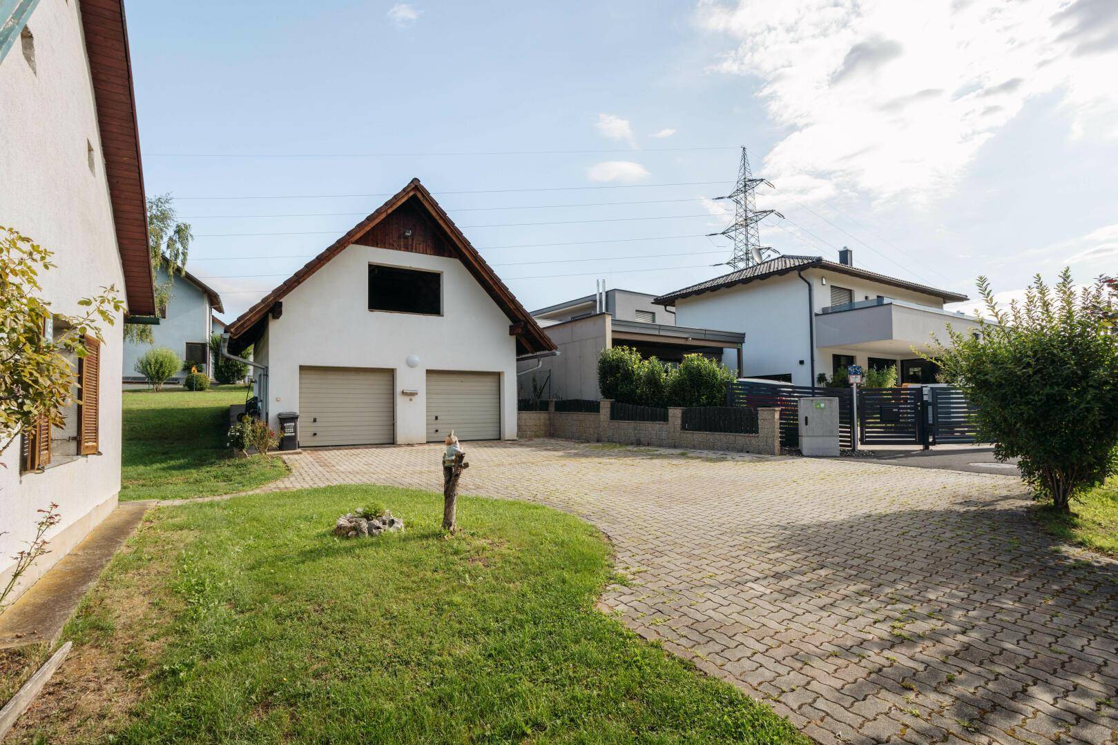 Gepflasterte Auffahrt zu einem Garagengebäude mit weiteren Häusern im Hintergrund.