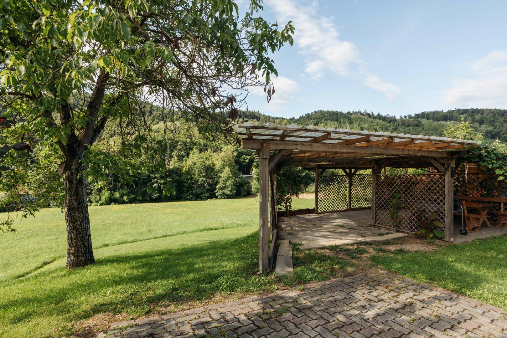 Hölzerner Carport mit gepflastertem Bereich und Blick auf die umliegende Natur.