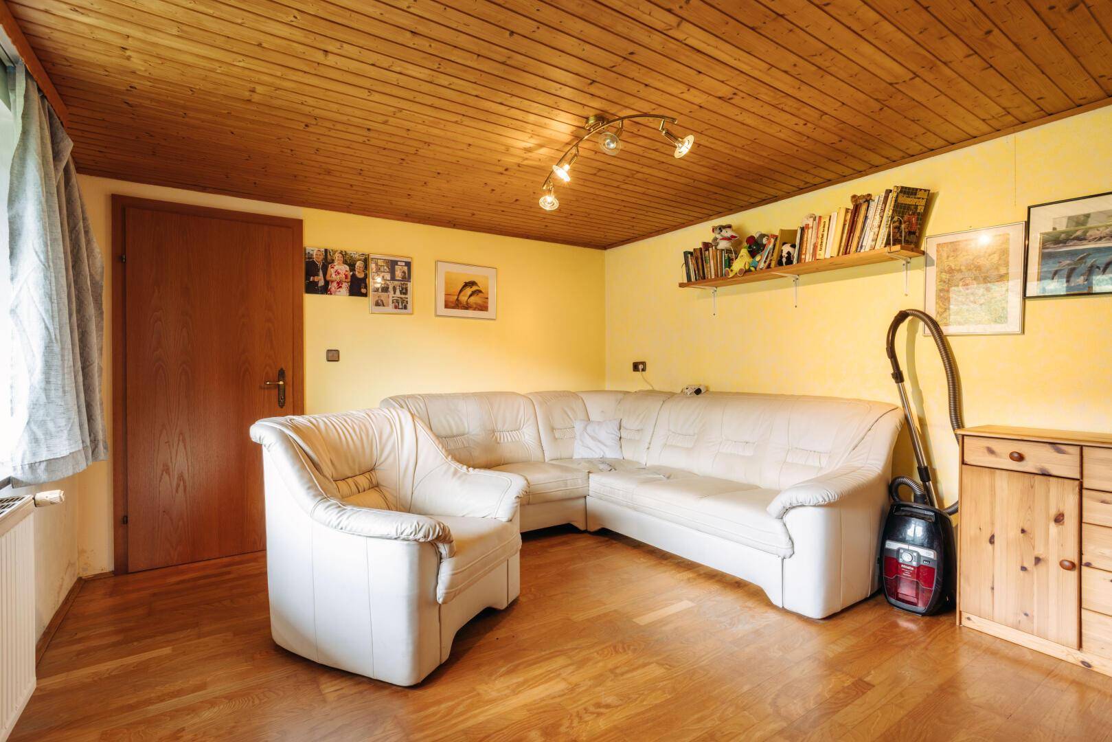 Gemütliches Wohnzimmer mit Holzdecke, Parkettboden und bequemer Eckcouch.