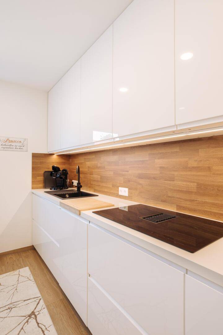 Detailansicht der modernen Küche mit Induktionskochfeld, Spüle und Holzrückwand.