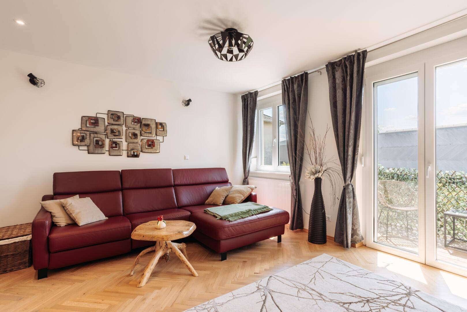 Gemütliches Wohnzimmer mit rotem Ledersofa, Holztisch und Zugang zum Balkon.