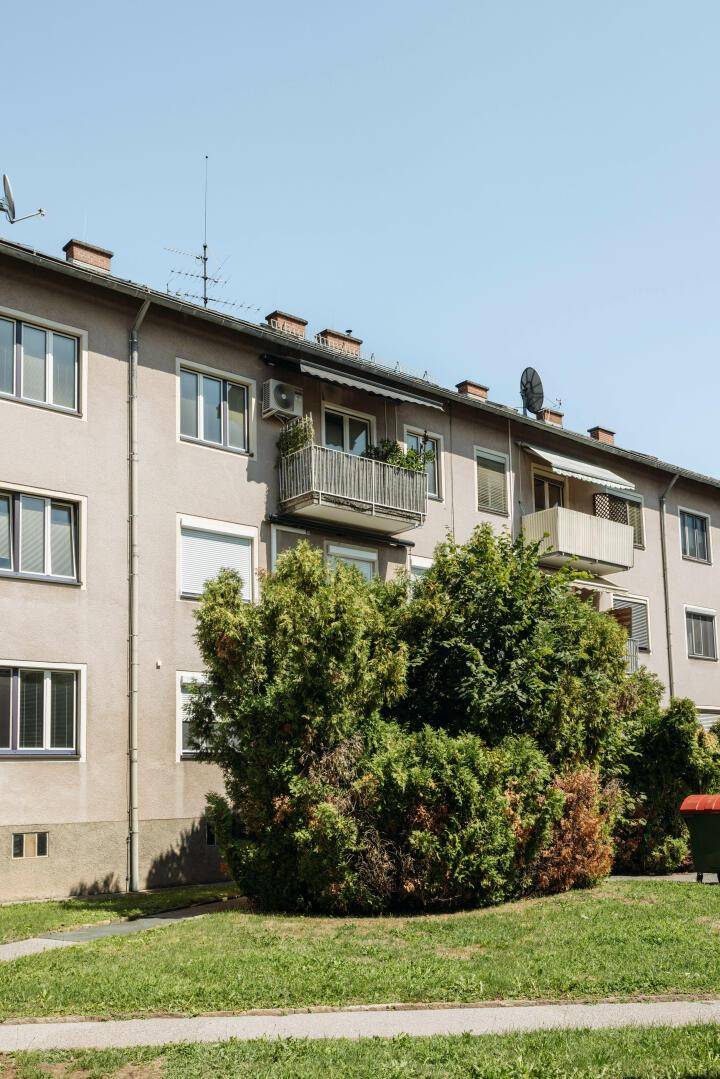 Mehrfamilienhaus mit Balkonen und grüner Umgebung an einem sonnigen Tag.