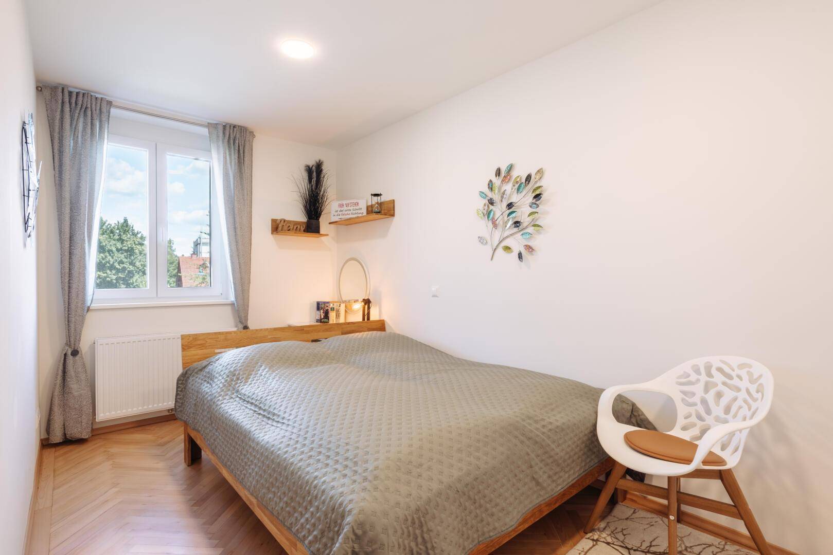 Helles Schlafzimmer mit Holzbett, Parkettboden und Fenster mit Blick ins Grüne.
