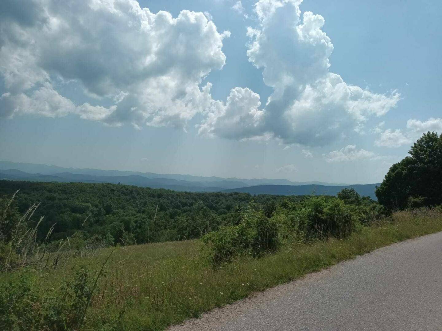Weitläufige grüne Landschaft mit bewaldeten Hügeln und einem weiten Himmel mit Wolken.