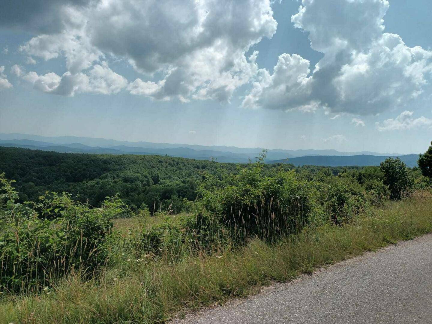 Weitläufige grüne Landschaft mit bewaldeten Hügeln und einem weiten Himmel mit Wolken.