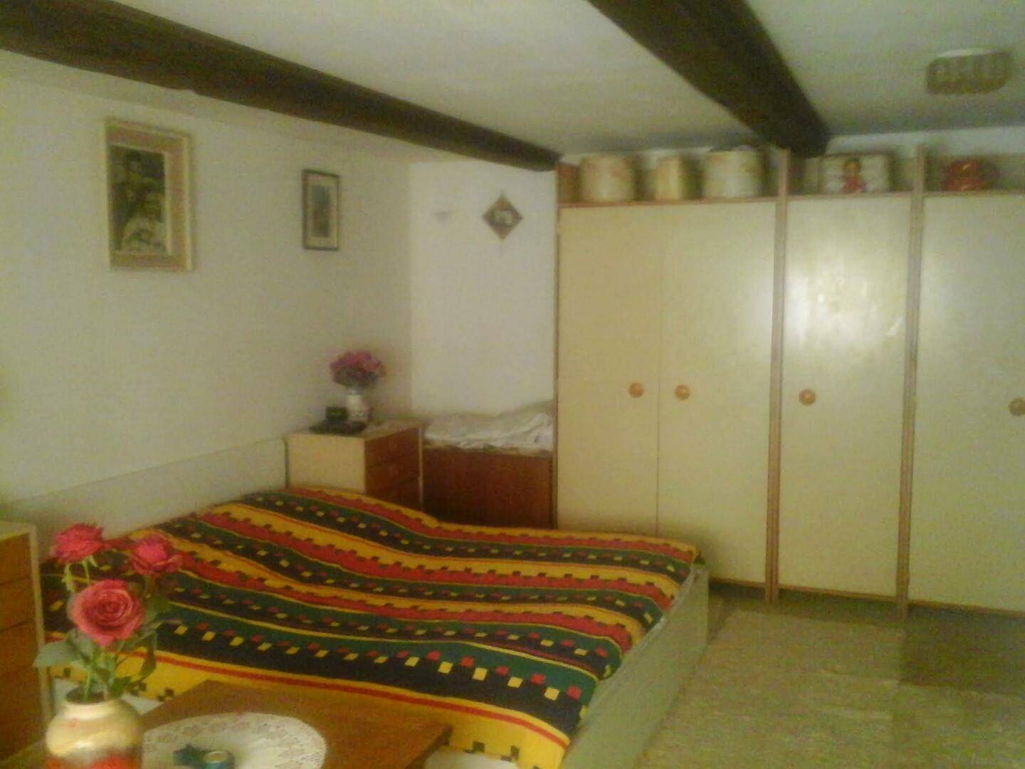 Schlafzimmer mit einem großen Bett, bunten Textilien und weißen Einbauschränken unter Holzbalken.