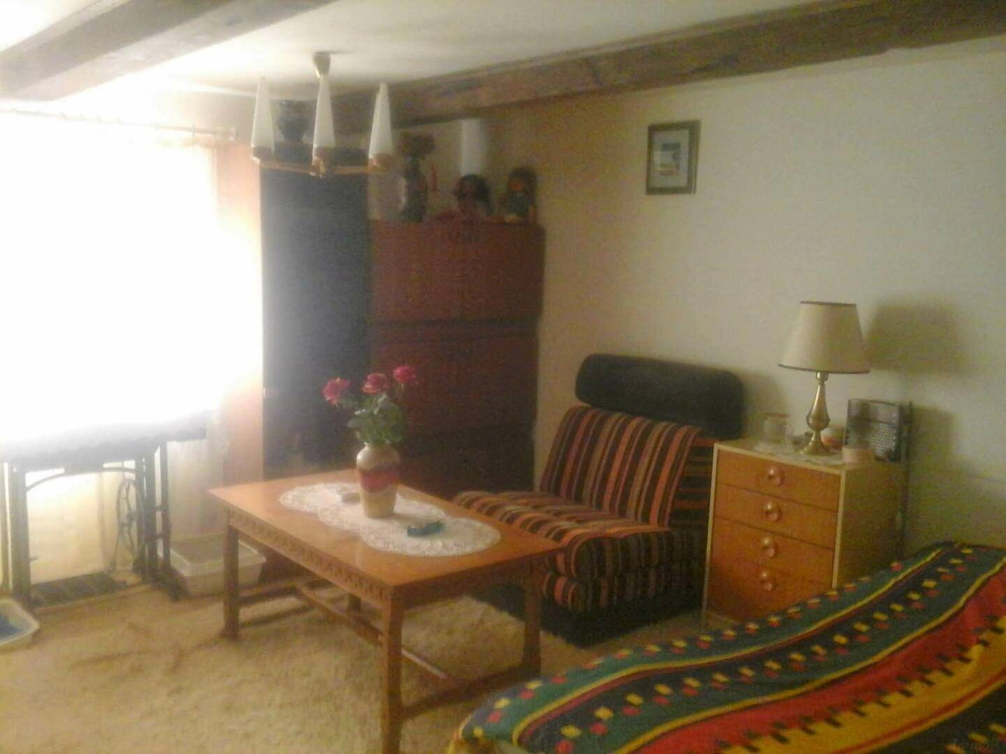 Schlafzimmer mit Holzbalken an der Decke, einem bunten Bettüberwurf und einem Holztisch.