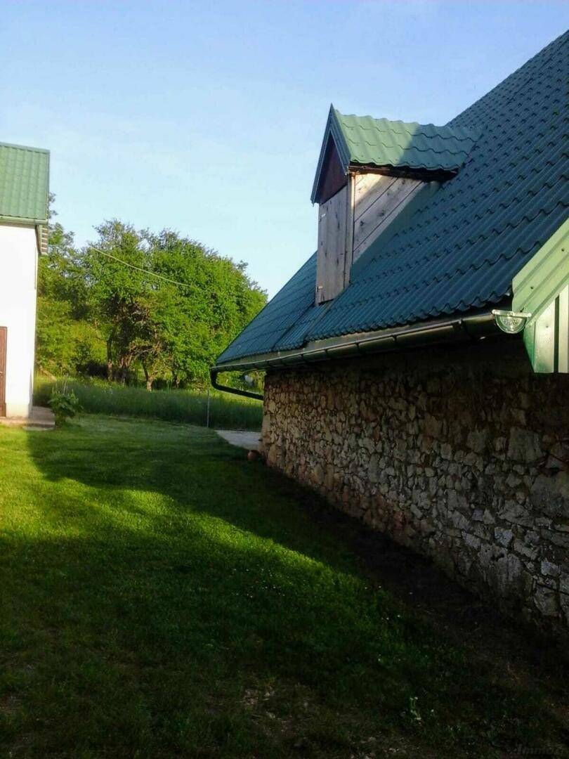 Seitenansicht eines Hauses mit einer rustikalen Steinmauer und einem grünen Wellblechdach.