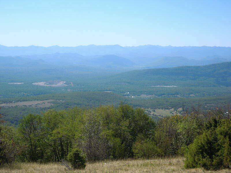 Weitläufiger Blick über bewaldete Hügel und eine weite Landschaft unter klarem, blauem Himmel.